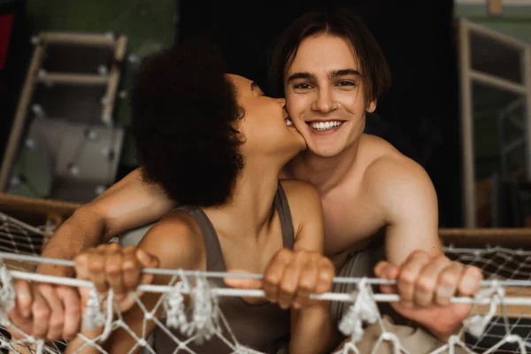 Sexy african american woman kissing happy shirtless boyfriend looking at camera from hammock — Stock Photo