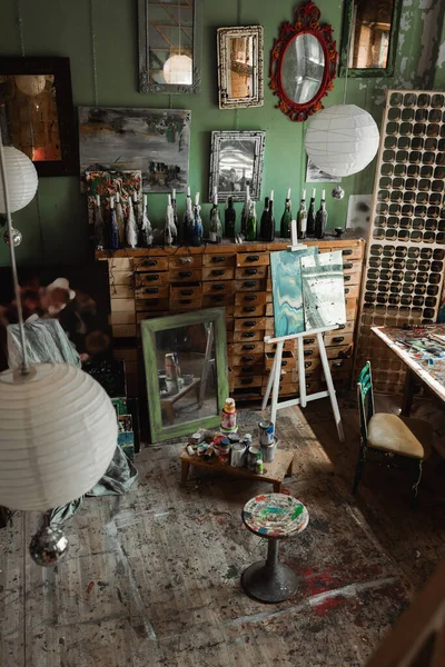 Art studio with vintage furniture and mirrors with paintings on wall near easel and cans with paints — Stock Photo