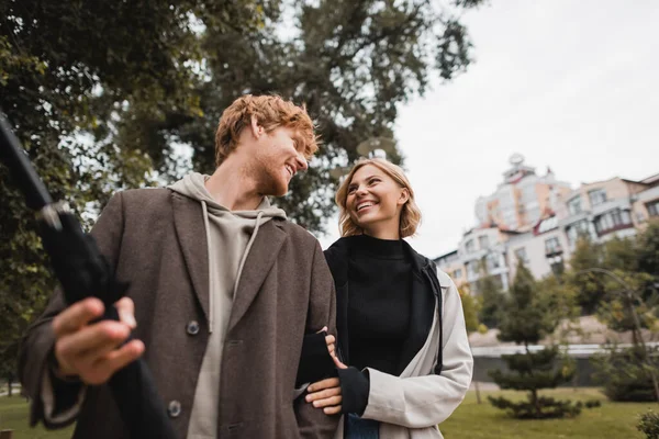 Happy redhead man and joyful blonde woman looking at each other while walking in park — Stock Photo