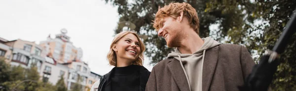 Happy redhead man and joyful blonde woman looking at each other while walking in park, banner — Stock Photo