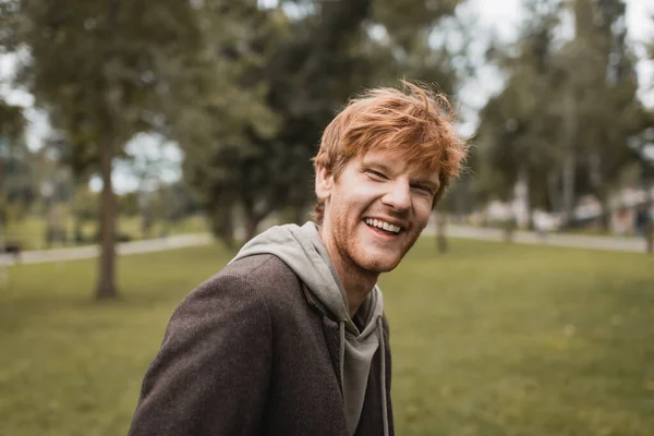 Cheerful and redhead man in autumnal outfit smiling in park — Stock Photo