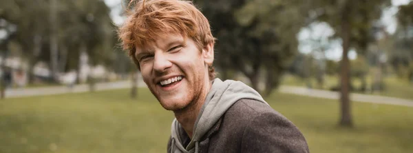 Cheerful and redhead man in autumnal outfit smiling in park, banner — Stock Photo