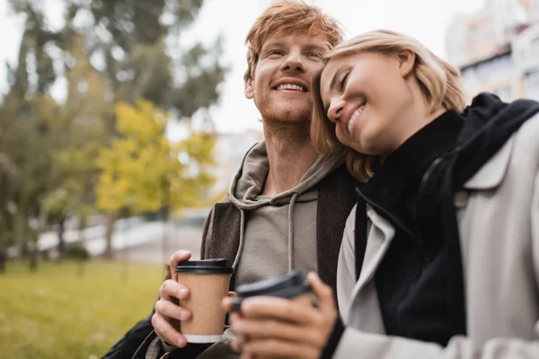 Feliz pareja joven sosteniendo tazas de papel con café para ir en el parque - foto de stock