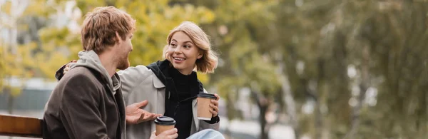 Sorrindo jovem casal conversando e segurando copos de papel com café para ir, banner — Fotografia de Stock