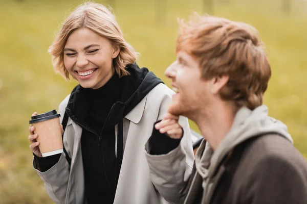Happy blonde woman holding paper cup and touching chin of redhead boyfriend — Stock Photo