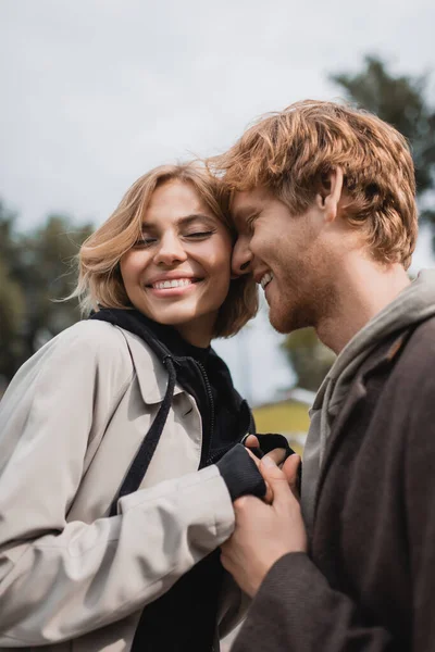 Feliz pelirroja hombre y rubia mujer sonriendo mientras toma de la mano al aire libre - foto de stock