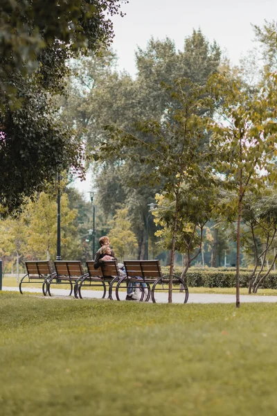 Happy young man and woman hugging and sitting on wooden bench in green park — Stock Photo