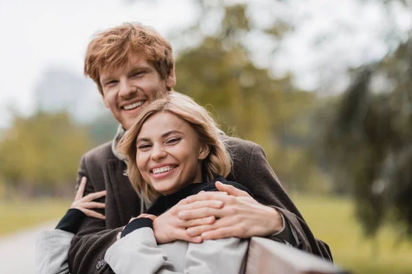 Cheerful young man hugging positive woman in green park — Stock Photo