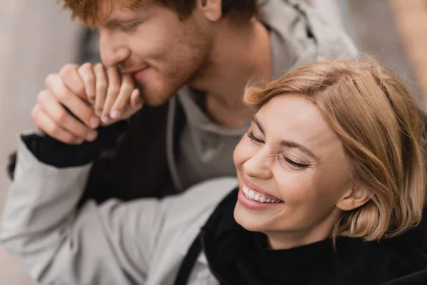 Vista ad alto angolo di rossa uomo baciare la mano di felice ragazza bionda all'aperto — Foto stock