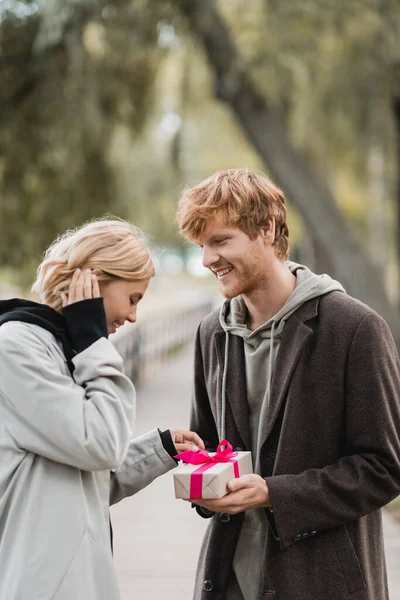 Heureux rousse homme tenant enveloppé présent près heureux petite amie dans le parc — Photo de stock