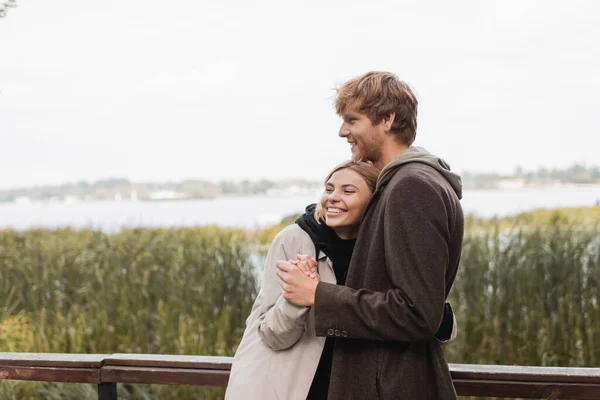 Redhead man hugging and holding hand of cheerful blonde woman during date in park — Stock Photo