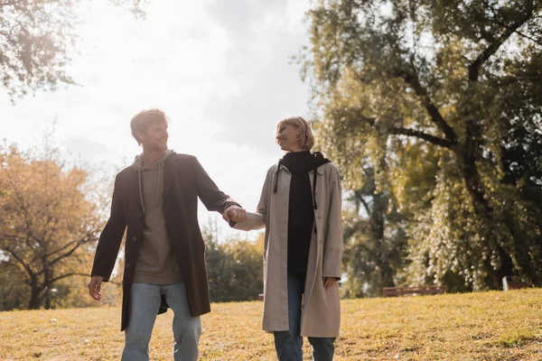 Coppia giovane e felice che si guarda mentre si tiene per mano nel parco autunnale — Foto stock