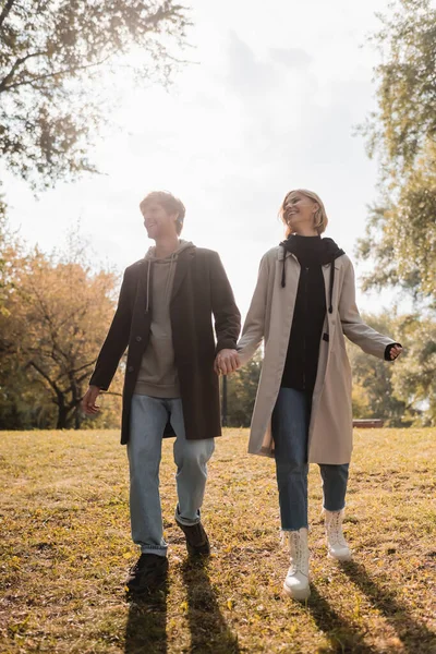 Full length of young and happy couple holding hands while walking in autumnal park — Stock Photo