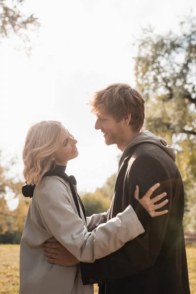 Vue latérale du jeune et joyeux couple souriant tout en s'embrassant dans le parc automnal — Photo de stock