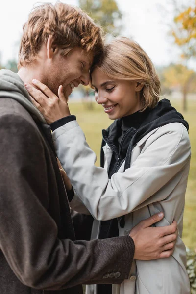 Joyful young couple with closed eyes embracing in autumnal park during date — Stock Photo