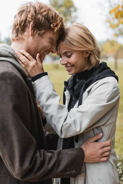 Joyeux jeune couple avec les yeux fermés embrassant dans le parc automnal pendant la date — Photo de stock