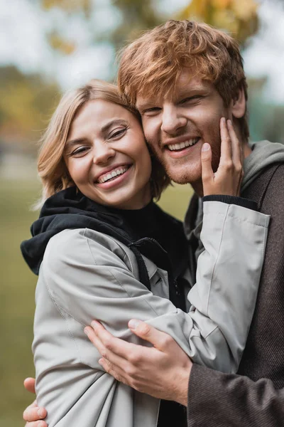 Porträt eines glücklichen Paares in Mänteln, das beim Date in die Kamera schaut und sich umarmt — Stockfoto