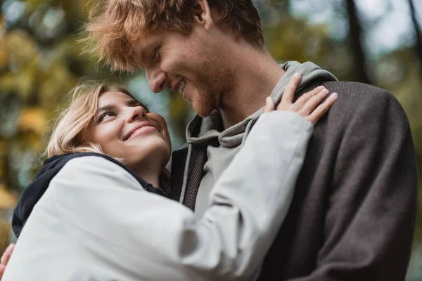Visão de baixo ângulo de casal feliz em casacos olhando um para o outro enquanto abraçando durante a data — Fotografia de Stock