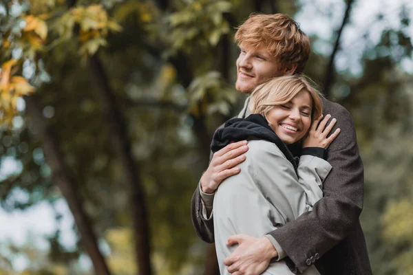 Feliz pareja joven en abrigos otoñales abrazándose entre sí durante la fecha - foto de stock