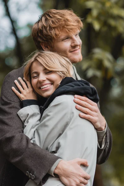 Cheerful and young couple in autumnal coats embracing each other during date — Stock Photo