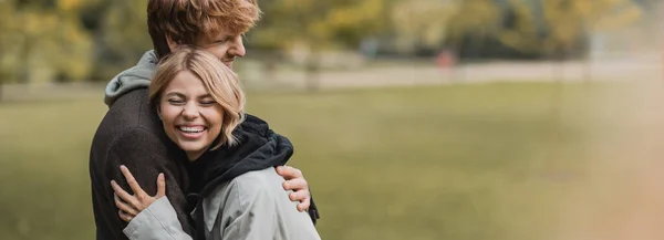 Allegro uomo e donna in cappotti autunnali che si abbracciano durante la data nel parco, striscione — Foto stock