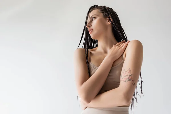 Vista a basso angolo della donna tatuata in biancheria intima guardando altrove isolata sul grigio — Foto stock