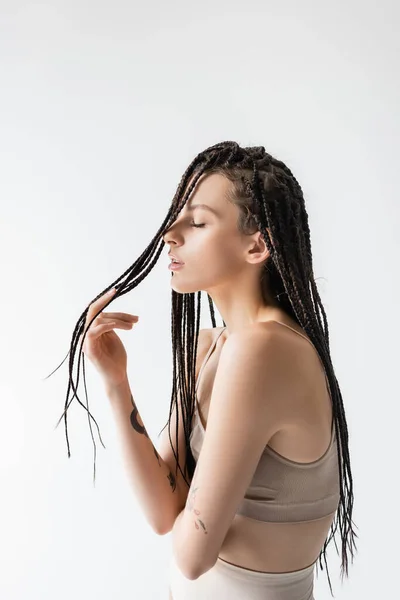 Вид збоку молодої жінки в спортивному бюстгальтері торкаються коси ізольовані на сірому — стокове фото