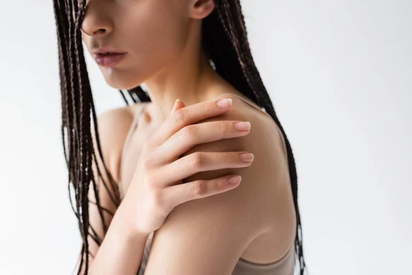 Vista recortada de mujer joven con trenzas tocando hombro aislado en gris - foto de stock