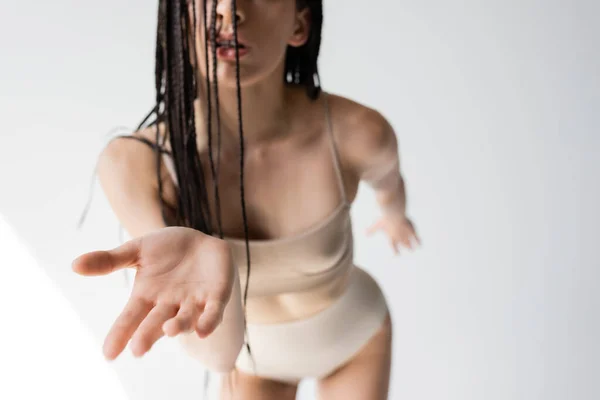 Cropped view of woman in blurred underwear outstretching hand on grey background — Stock Photo