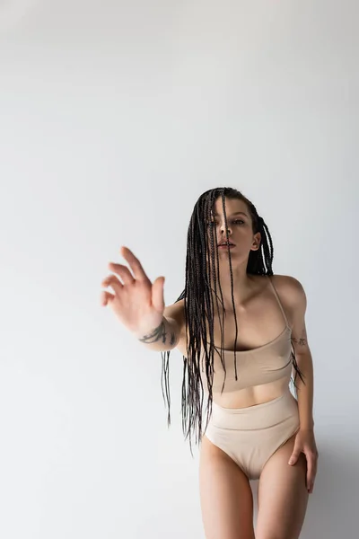 Mujer en forma con trenzas extendiendo la mano a la cámara sobre fondo gris - foto de stock