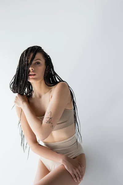 Sexy woman in underwear touching braids and looking at camera on grey background — Stock Photo