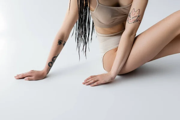 Vista ritagliata della donna tatuata in biancheria intima toccare sfondo grigio — Foto stock