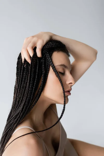 Young woman with braids and sports bra touching head isolated on grey — Stock Photo