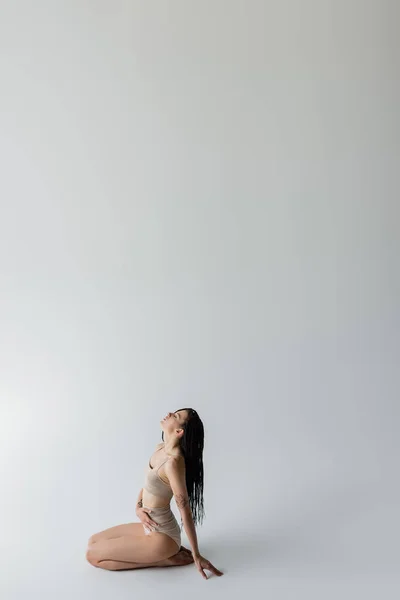 Side view of young fit woman in underwear sitting on grey background — Stock Photo