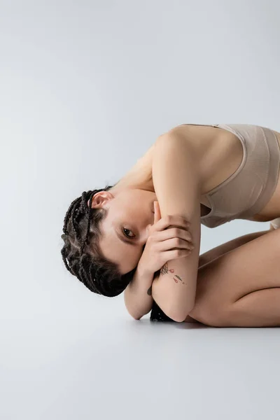 Jeune femme en soutien-gorge de sport regardant la caméra tout en posant sur fond gris — Photo de stock