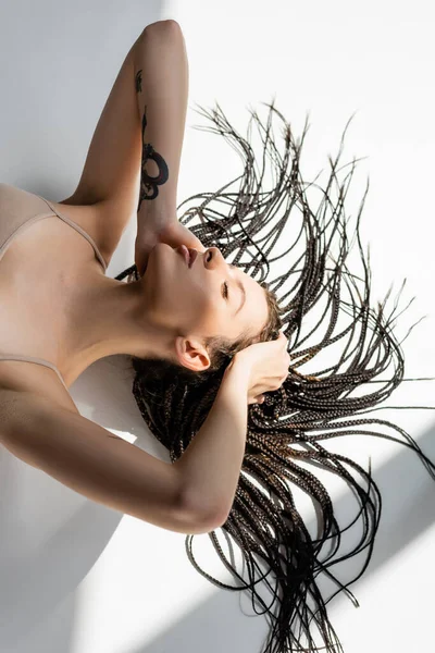 Draufsicht der brünetten Frau mit Zöpfen liegend auf grauem Hintergrund mit Licht — Stockfoto