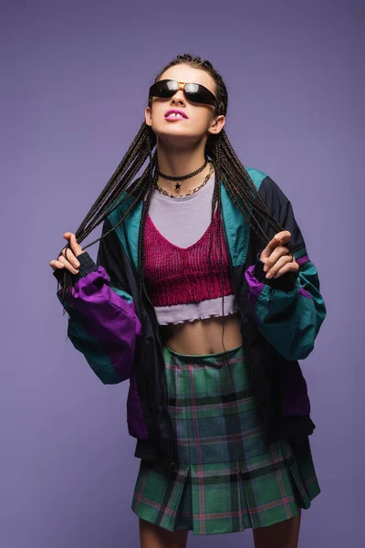 Mujer joven en ropa vintage y gafas de sol de pie aislado en púrpura - foto de stock