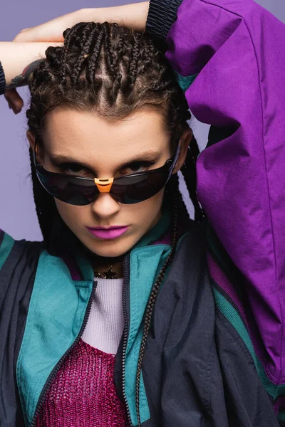 Portrait de jeune modèle élégant en lunettes de soleil rétro regardant la caméra isolée sur violet — Photo de stock