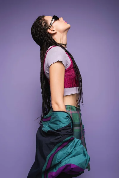 Side view of nineties style woman in sunglasses posing with raised head isolated on purple — Stock Photo