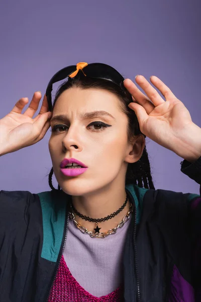 Portrait of young woman with makeup holding sunglasses and looking at camera isolated on purple — Stock Photo