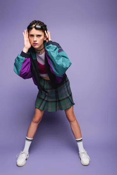 Full length of tense woman in casual nineties outfit and white sneakers touching head on purple background — Stock Photo