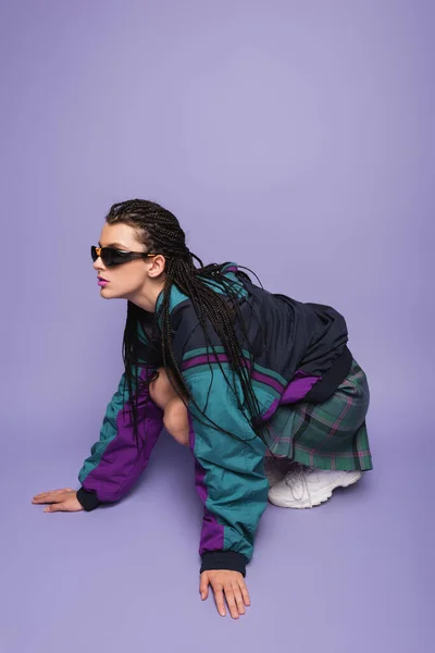 Mulher com dreadlocks posando em jaqueta vintage e óculos de sol no fundo roxo — Fotografia de Stock