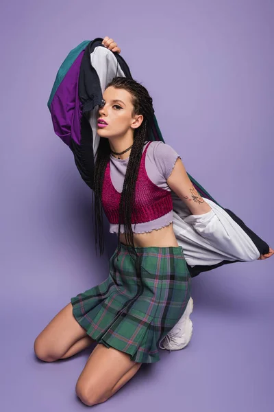 Brunette woman in plaid skirt posing with vintage style jacket on purple background — Stock Photo