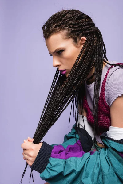 Young woman in vintage clothes touching braided dreadlocks isolated on purple — Stock Photo