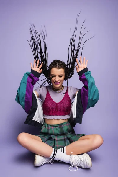 Happy nineties style woman sitting with crossed legs on purple background — Stock Photo