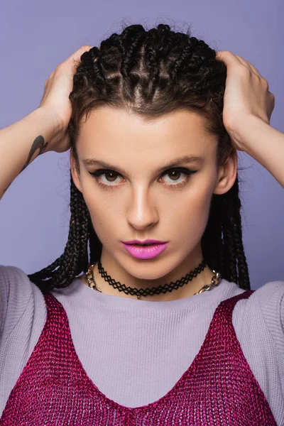 Retrato de mulher bonita na maquiagem tocando o cabelo trançado enquanto olha para a câmera isolada no roxo — Fotografia de Stock