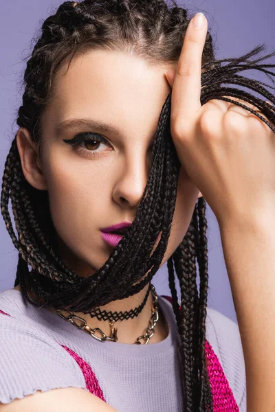 Portrait of young woman obscuring face with braids and looking at camera isolated on purple — Stock Photo