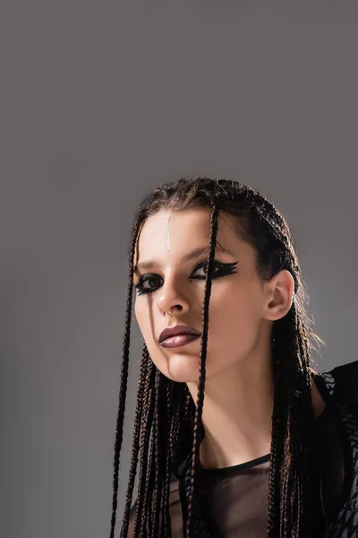 Ritratto di giovane donna con trucco futuristico e dreadlocks intrecciati guardando la fotocamera isolata su grigio — Foto stock