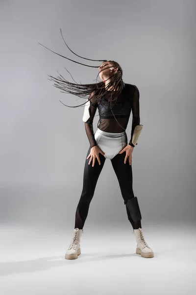 Longitud completa de la mujer en forma con rastas posando en mono negro y pantalones cortos de plata sobre fondo gris - foto de stock