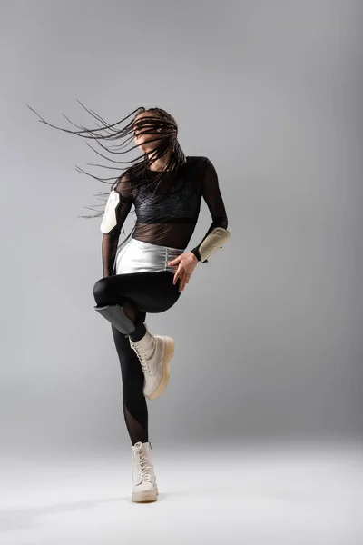 Mujer con rastas trenzadas posando en botas blancas y atuendo futurista sobre fondo gris - foto de stock